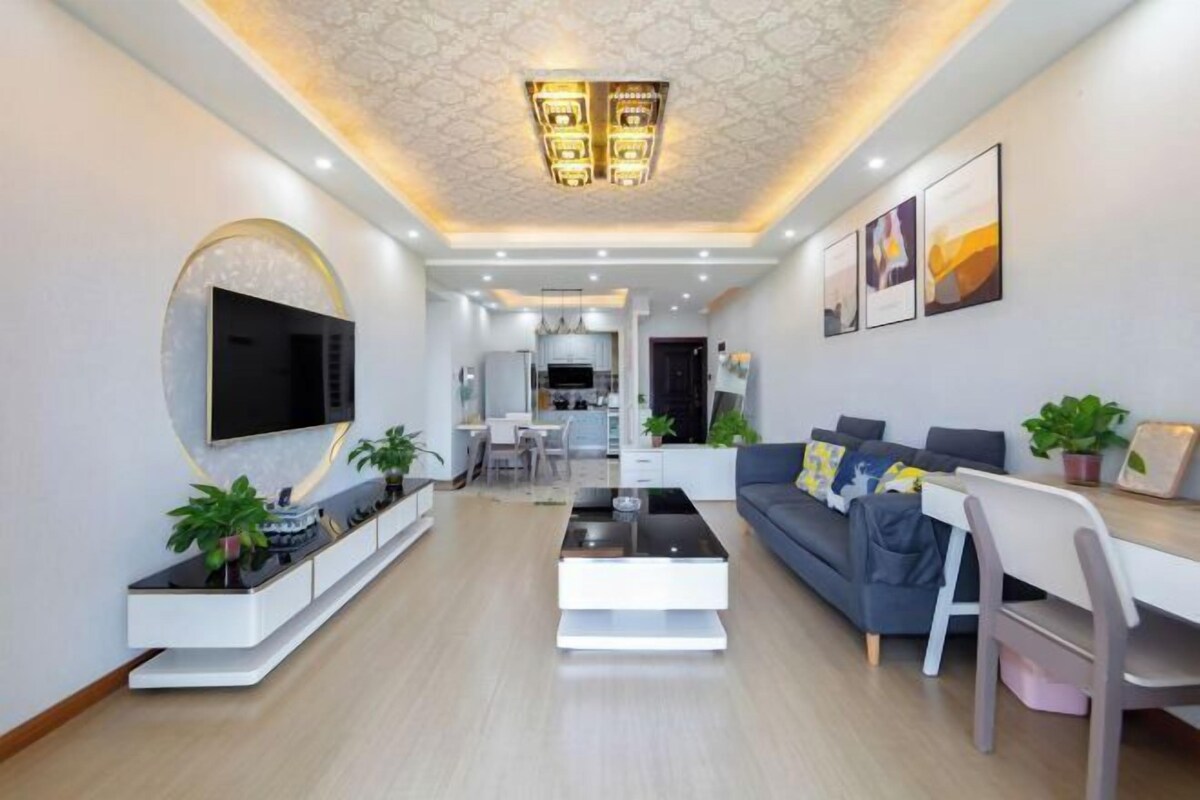 Una sala de estar moderna con un televisor de pantalla plana, un sofá, una mesa de centro y una zona de comedor con una mesa y sillas blancas.