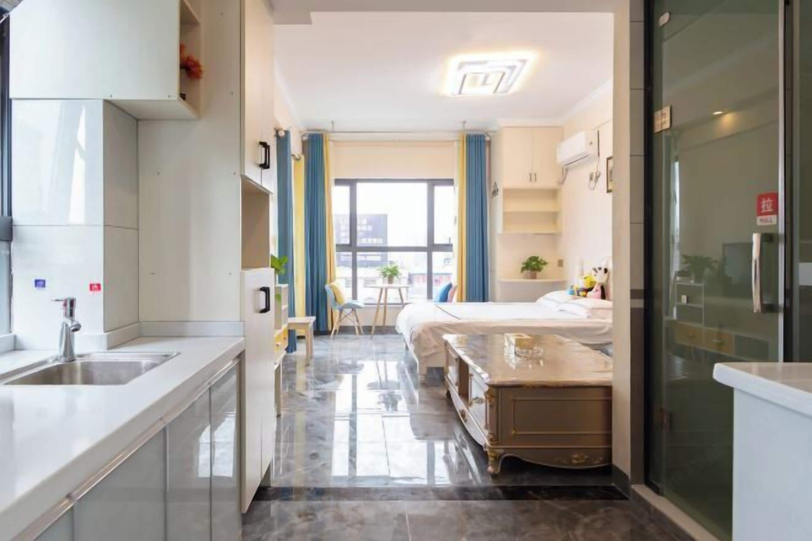 A modern hotel room with a kitchen area, a dining table, and a bed.
