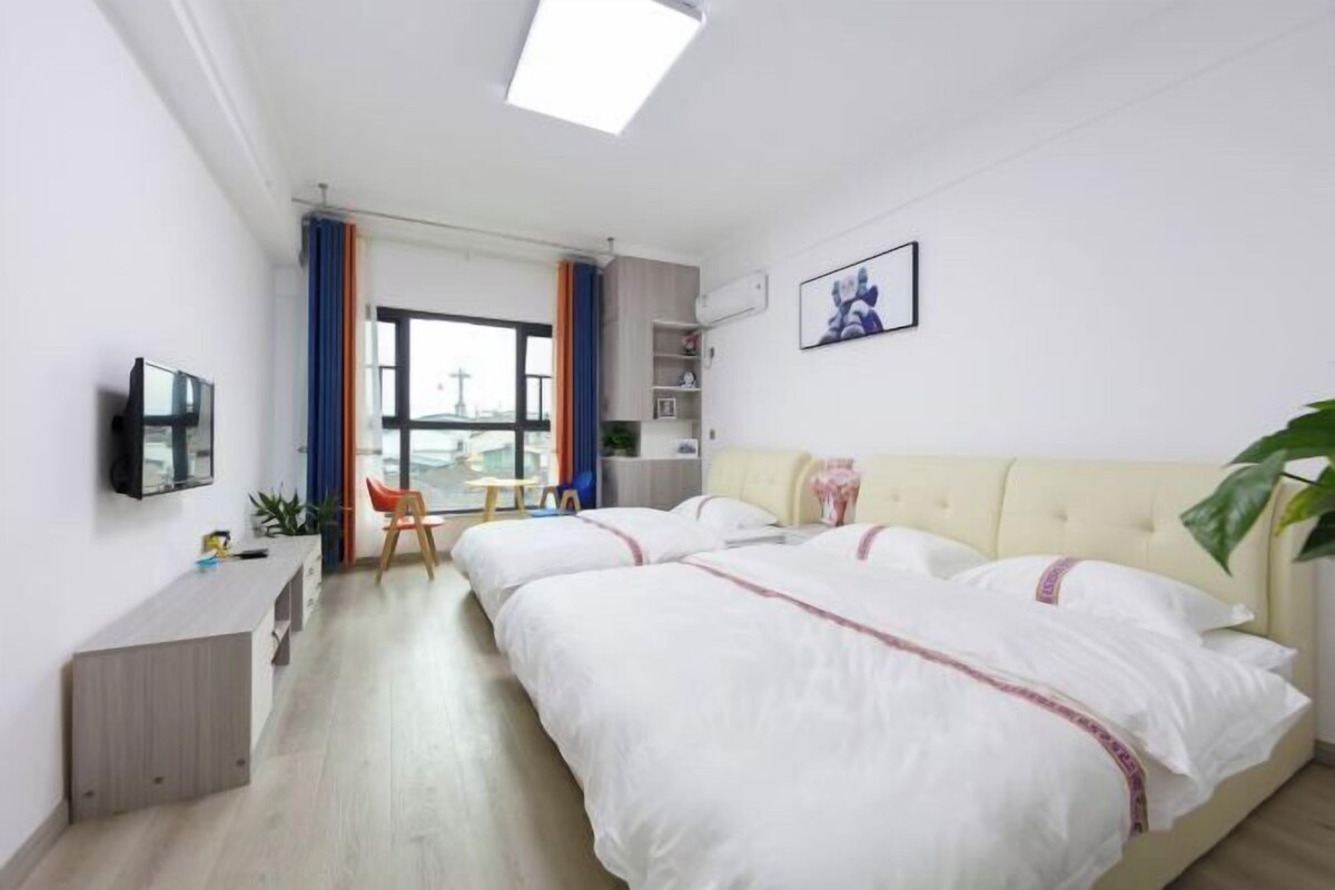Habitación de hotel con dos camas, televisor, escritorio y ventana con cortinas.