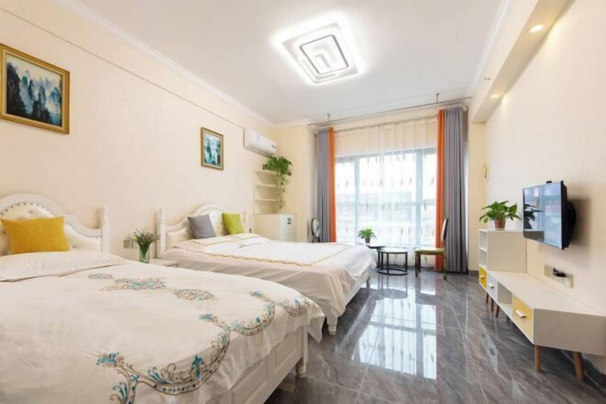 A hotel room with two beds, a TV, a desk, and a window with curtains.