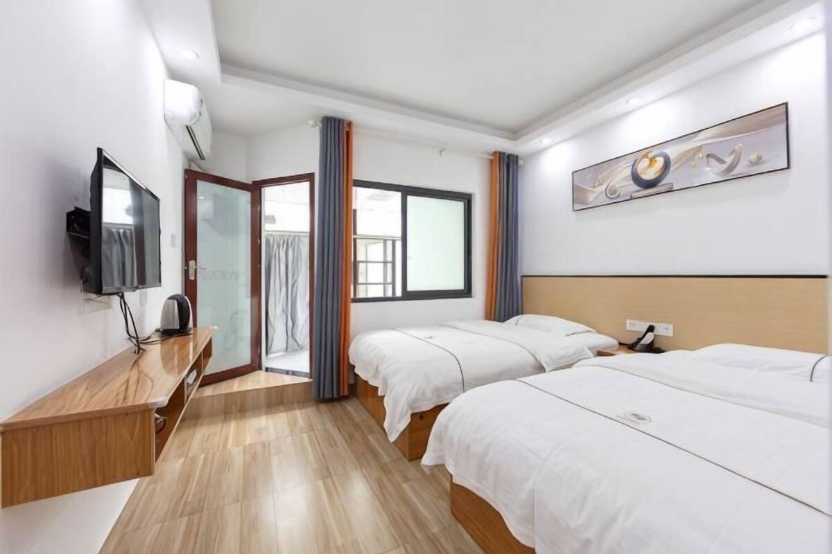 A hotel room with two beds, a TV, a desk, and a window.