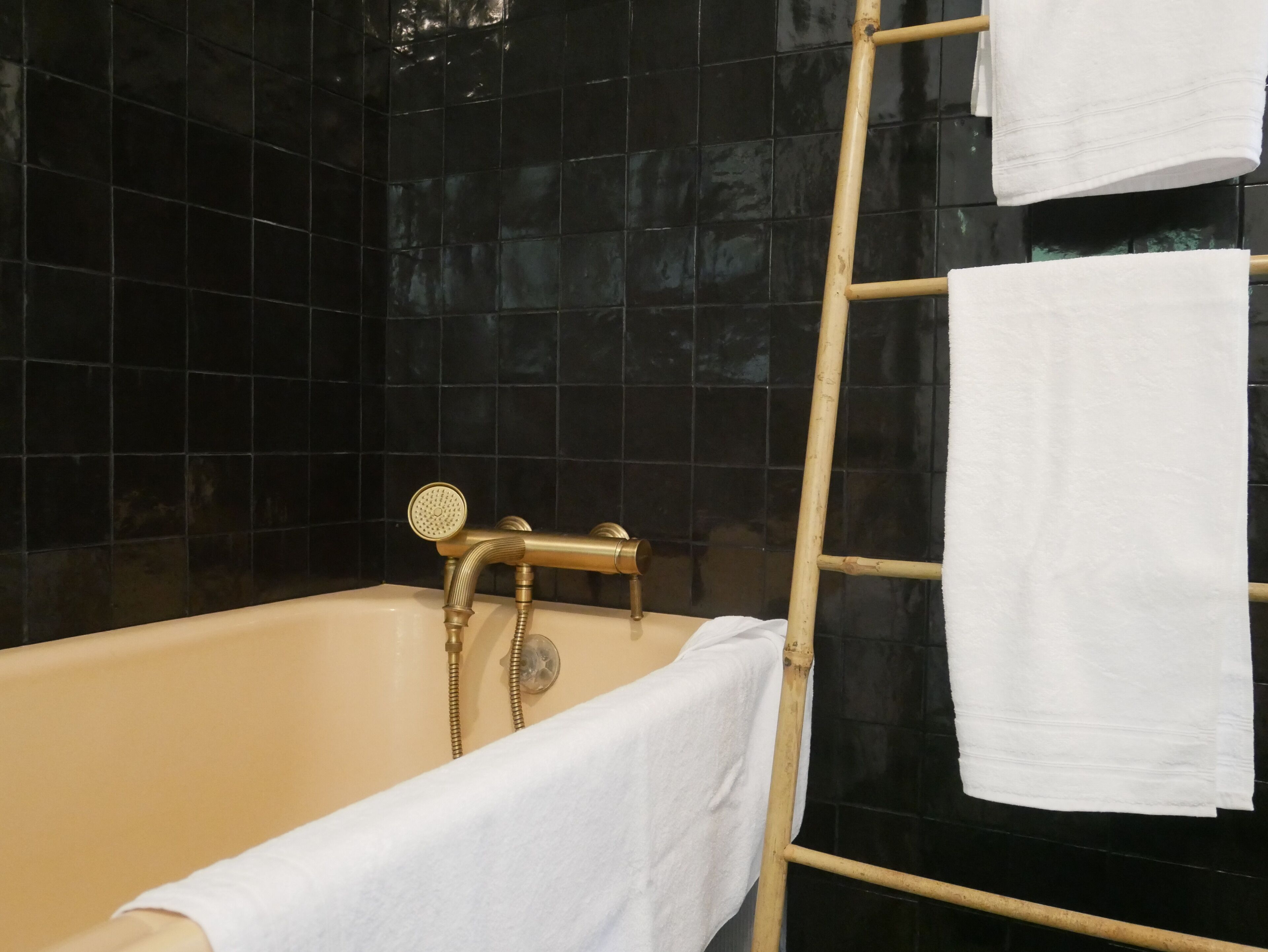 Een bad met een gouden kraan en een houten ladder die tegen de muur staat.