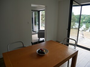 A dining area with a wooden table and chairs, a bowl of fruit, and a view of a garden through a glass door. - house with sea river view, with jacuzzi spa (Gouesnach)