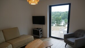 A living room with a sofa, a small table, a chair, a television, and a view of a natural landscape through a large window. - house with sea river view, with jacuzzi spa (Gouesnach)