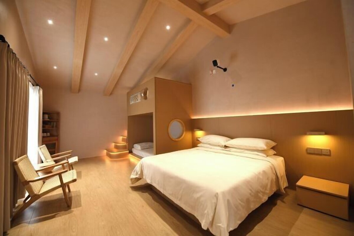 A modern bedroom with a large bed, a bedside table, a chair, and a ceiling fan.