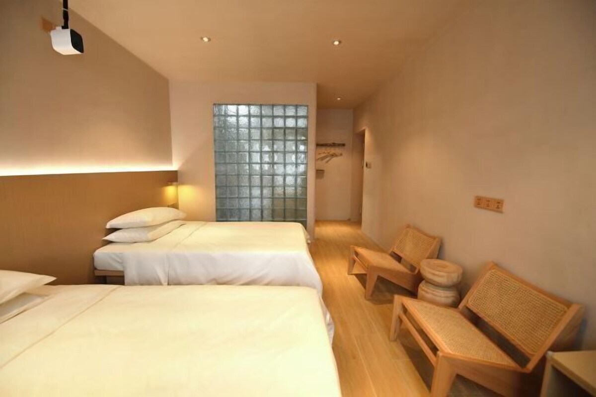 A hotel room with two beds, a large window with a view, wooden furniture, and a ceiling light.