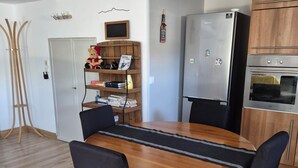 A dining area with a wooden table, black chairs, a bookshelf, a refrigerator, and a wooden cabinet. - self-contained 60m2 apartment in private grounds (Aubagne)
