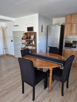Un coin repas comprenant une table en bois, des chaises noires, une bibliothèque, un réfrigérateur et un meuble en bois.