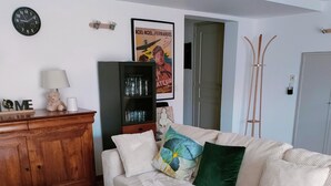 A living room with a sofa, a wooden side table, a lamp, a clock, a poster, and a bookshelf. - self-contained 60m2 apartment in private grounds (Aubagne)