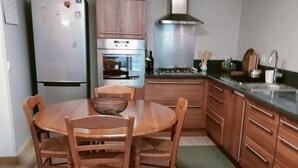 A compact kitchen with wooden cabinets, a built-in oven, a stainless steel range hood, and a dining table with four chairs. - self-contained 60m2 apartment in private grounds (Aubagne)