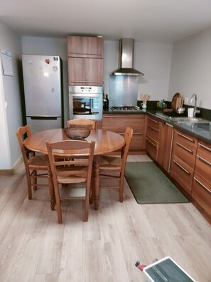 Une cuisine compacte avec des meubles en bois, un four encastré, une hotte de cuisine en acier inoxydable et une table à manger avec quatre chaises.