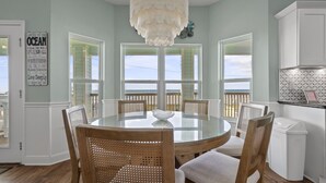 Un espace repas avec une table ronde en verre, des chaises en bois et un lustre blanc.