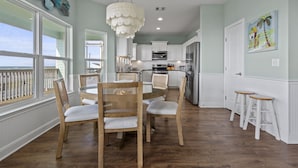 Une cuisine spacieuse avec des meubles blancs, un réfrigérateur en acier inoxydable et un coin repas comprenant des chaises en bois et une table en verre.