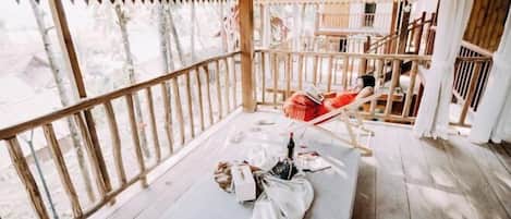 Una terraza de madera con una zona de estar acolchada, una botella y algunos objetos en el suelo.