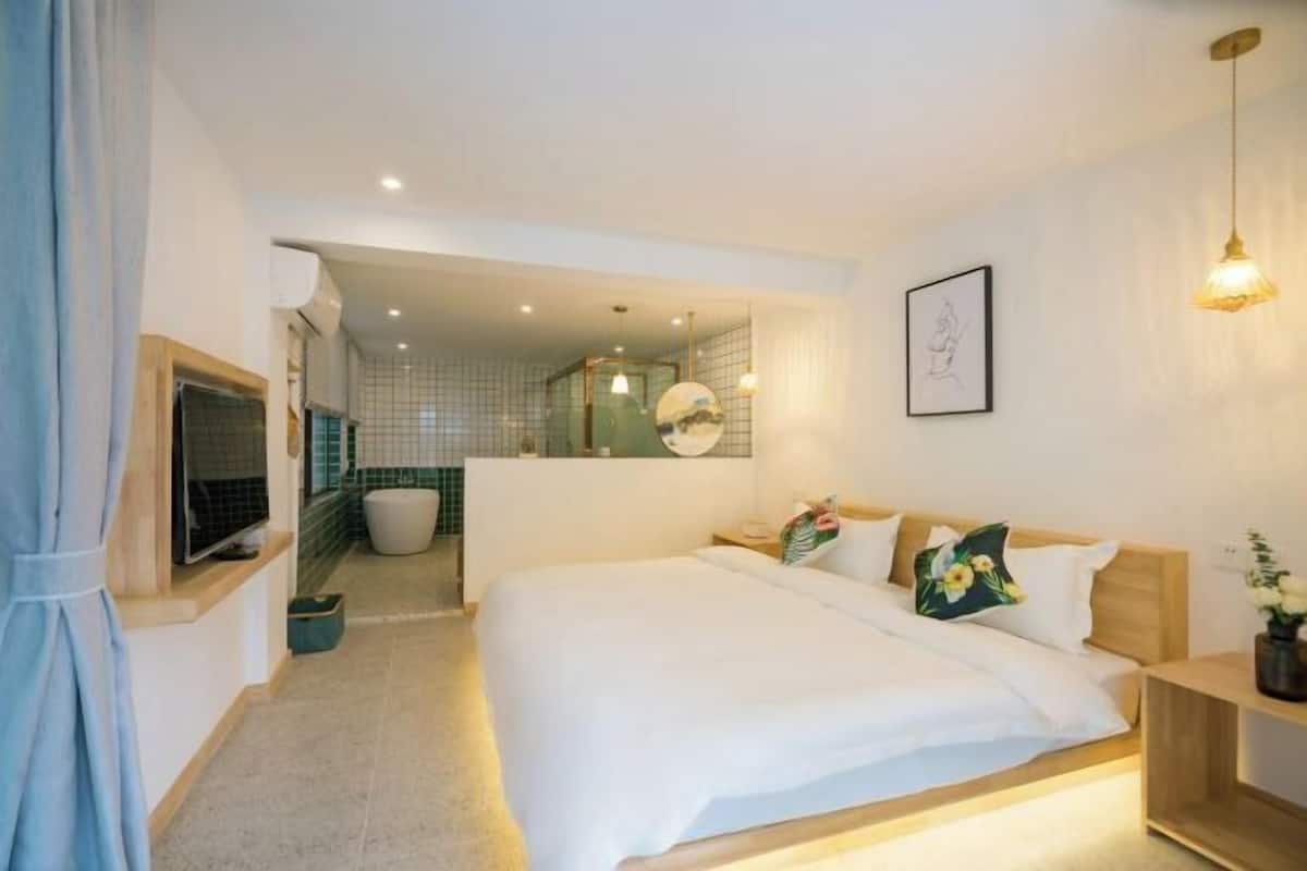 Een moderne slaapkamer met een groot bed, nachtkastjes, een televisie en een badkamer op de achtergrond.