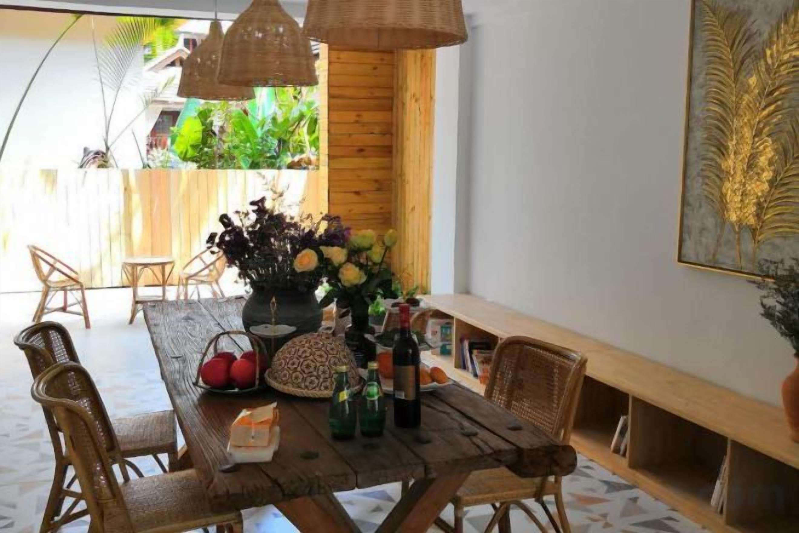 A dining area with a wooden table, wicker chairs, and a vase of flowers.