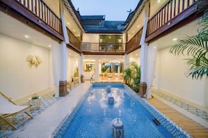 A courtyard with a central pool, wooden deck, and a covered seating area. - Lucky Clover Hotel (Jinghong)