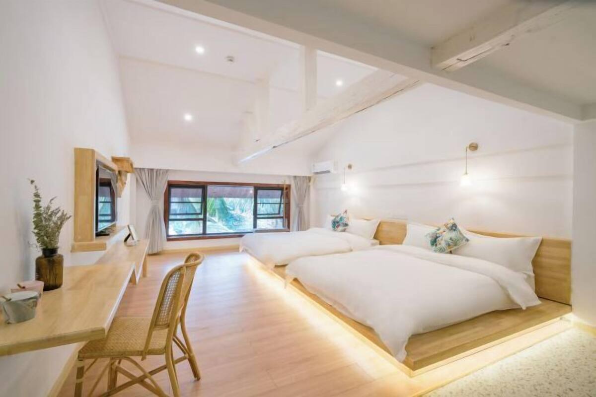 Een moderne slaapkamer met twee bedden, een houten bureau en een groot raam.