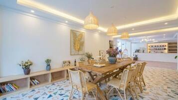 A dining area with a long wooden table, wicker chairs, pendant lighting, and a patterned floor.