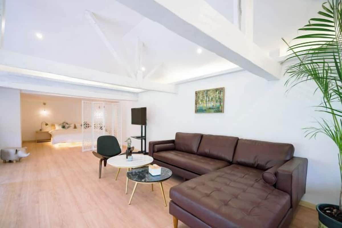 Een moderne woonkamer met een bruine leren bank, een ronde salontafel en een groene fauteuil. Aan de muur hangt een schilderij en er staat een potplant in de hoek.
