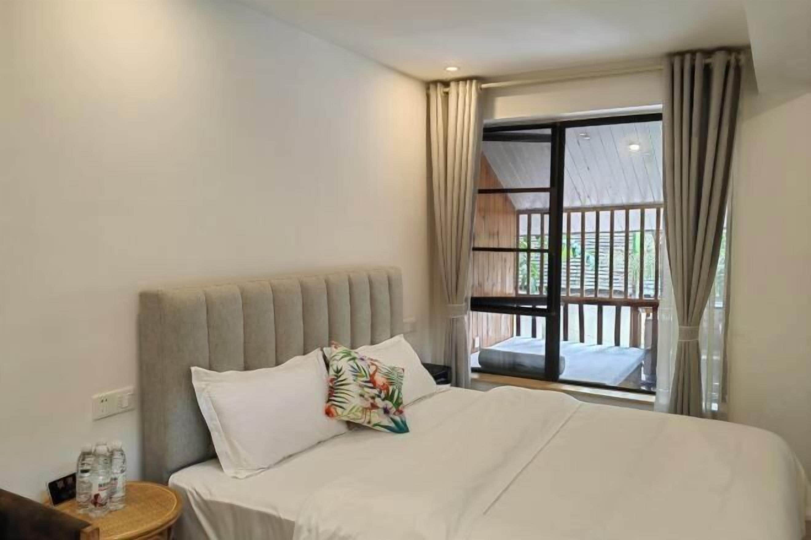 Habitación de hotel con cama, mesita de noche, ventana con cortinas y vista a un balcón.