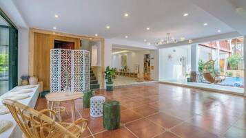 Um espaço interno amplo, com teto alto, área de estar com cadeiras de vime, um biombo decorativo e vista para um edifício.