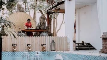 Área de piscina com deck de madeira, uma pessoa de camisa vermelha e um guarda-sol grande.