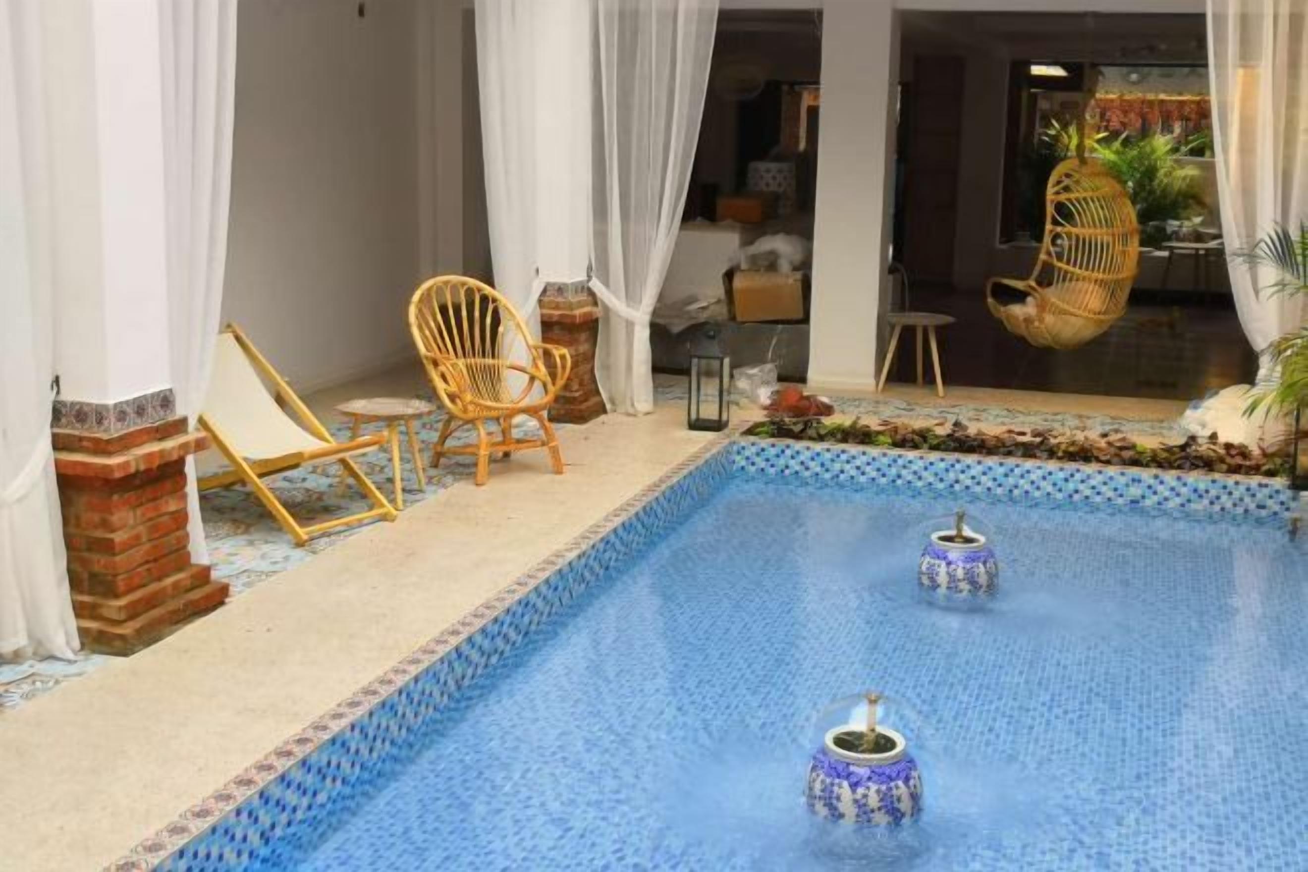 A pool with two decorative urns, surrounded by white curtains and wicker chairs.