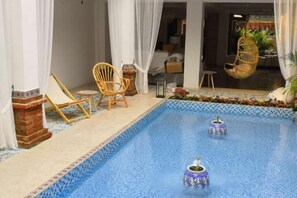 Une piscine agrémentée de deux vases décoratifs, entourée de rideaux blancs et de fauteuils en osier.