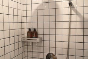 Une zone de douche carrelée, dotée d’un pommeau de douche à main et d’une étagère pour les articles de toilette.