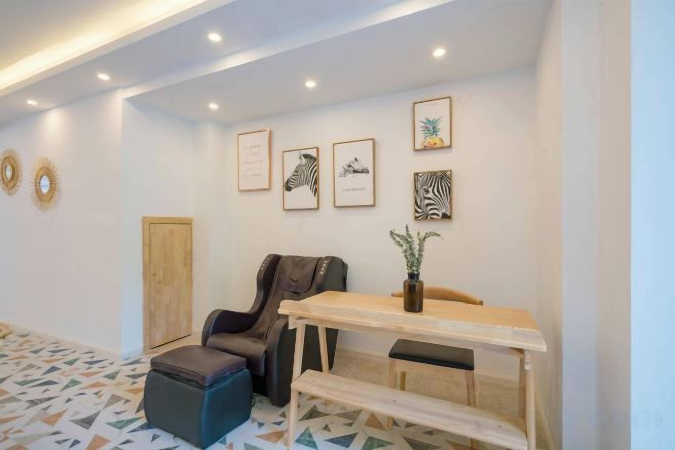 A room with a wooden desk, a chair, a bench, and a small table with a plant. There are framed pictures on the wall.