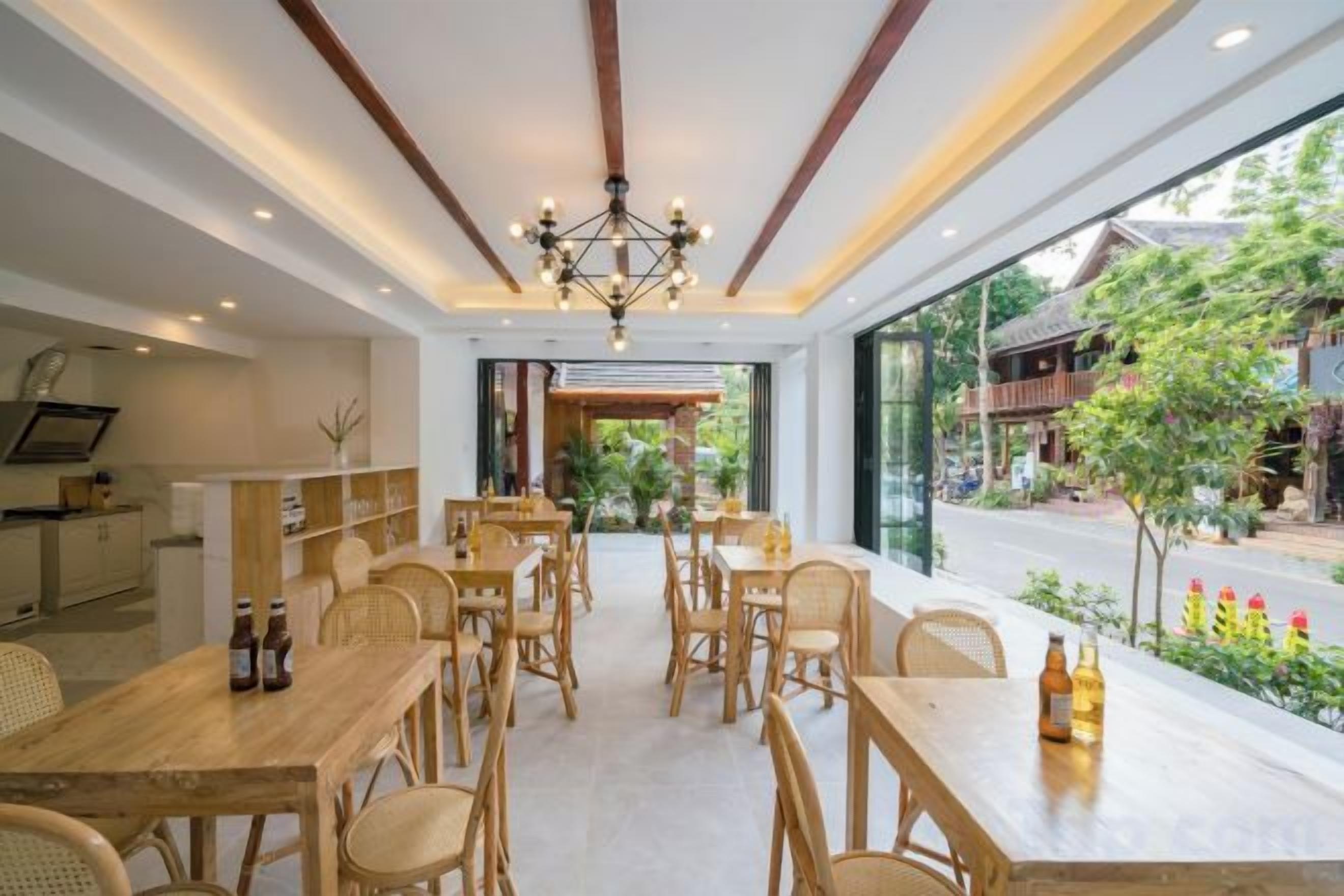 A dining area with wooden tables and chairs, a chandelier, and a view of the street outside.