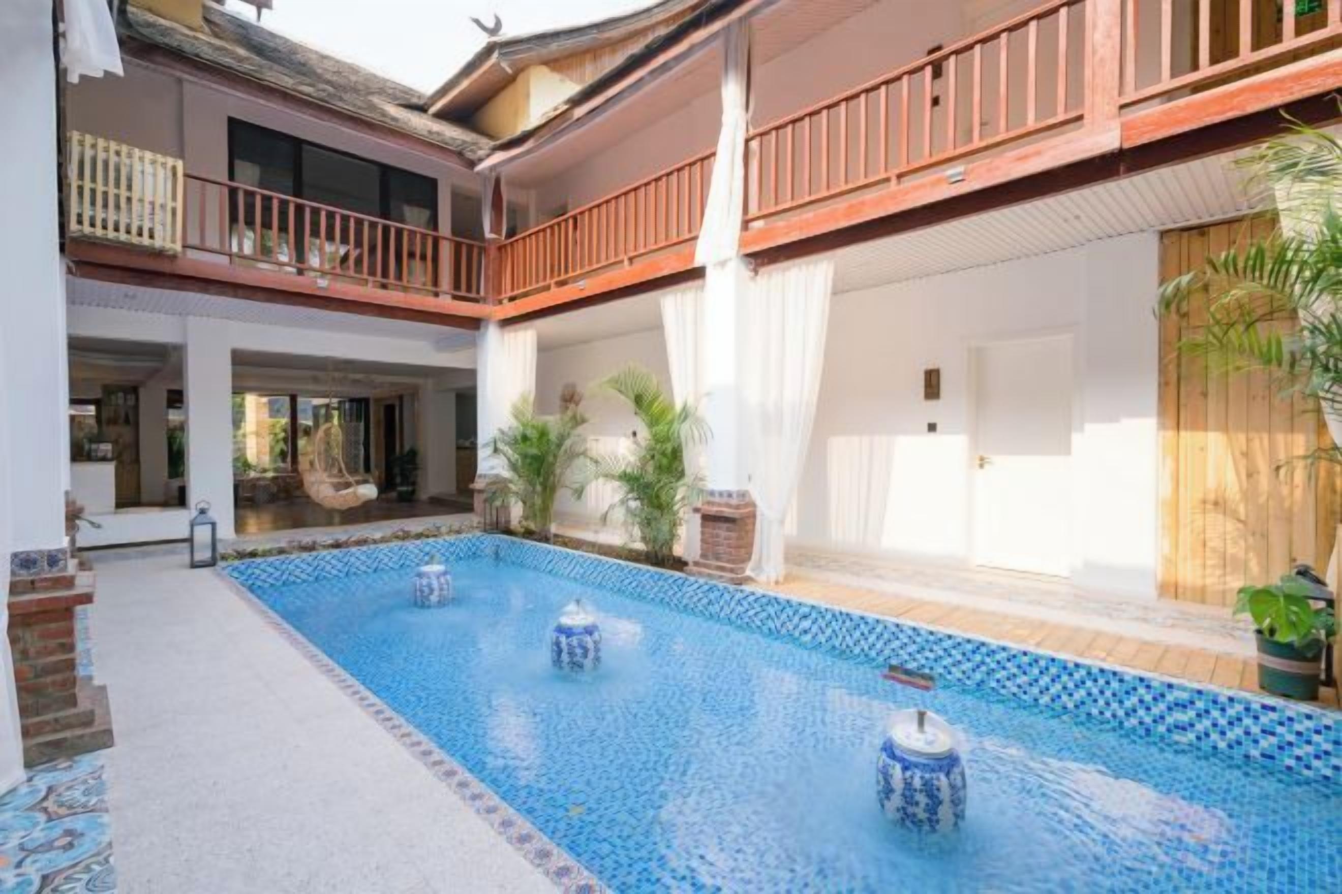 Una piscina con borde de azulejos, cubierta de madera y un balcón con barandilla.