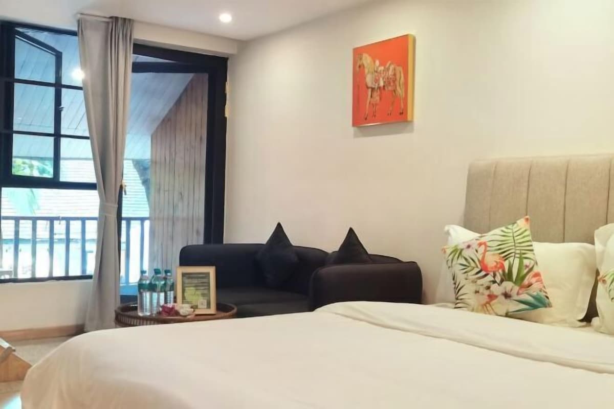 A hotel room with a bed, a sofa, a painting on the wall, and a window with curtains.
