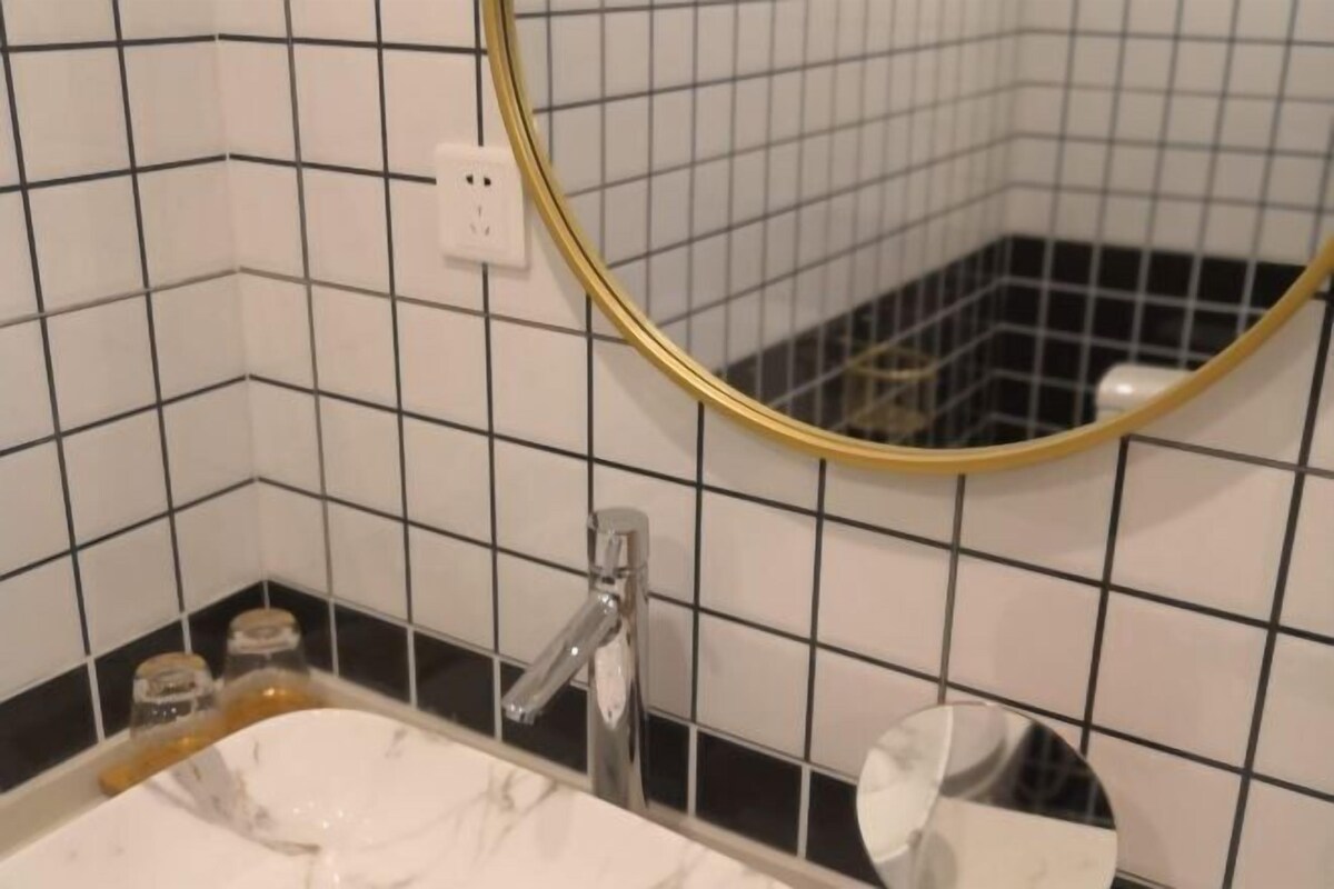 A bathroom with a white sink, a gold-framed mirror, and black and white tiled walls.
