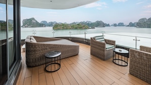 A deck with wicker furniture and a glass railing overlooking a body of water and islands. - Elite of the Seas (Tuan Chau)