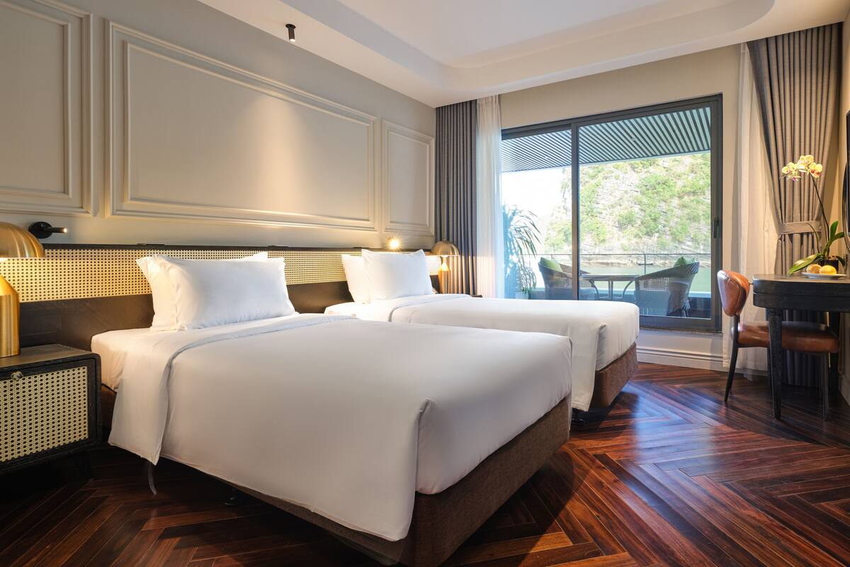 A hotel room with two beds, a large window with a view, a desk with a chair, and a TV.