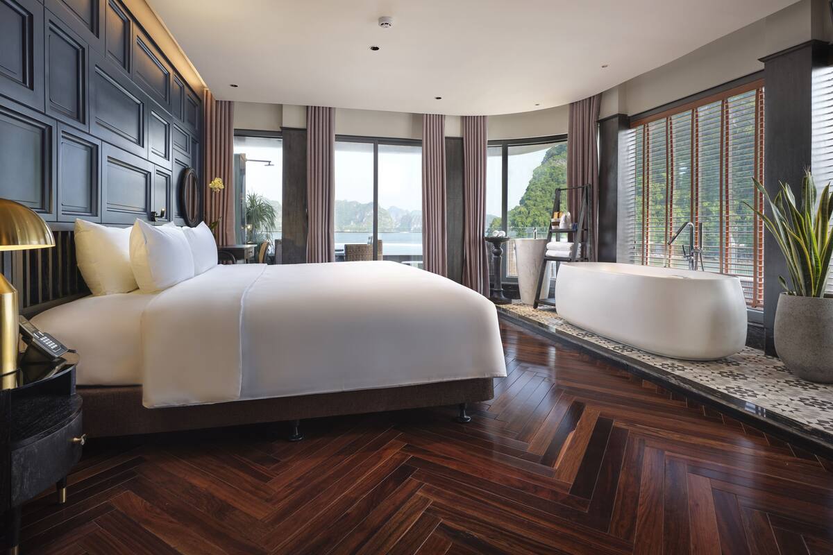 A modern hotel room with a large bed, a sitting area with a bathtub, and a view of the mountains.