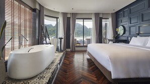 A modern hotel room with a large bathtub, a bed, and a view of mountains through large windows. - Elite of the Seas (Tuan Chau)