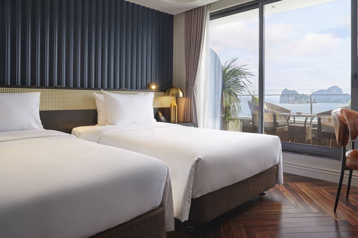 A hotel room with two beds, a view of the sea, and a balcony with outdoor furniture.