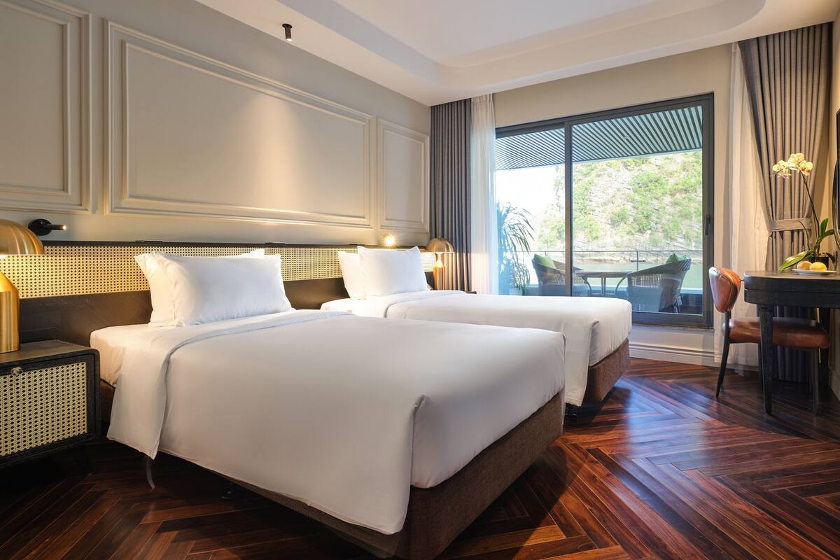 A hotel room with two beds, a desk, a chair, and a view of the outdoors.