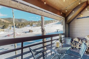 A balcony with a view of a snowy mountain landscape, a table with chairs, and a stack of firewood. - Best Ski in Ski out Location in Angel Fire! (Angel Fire)