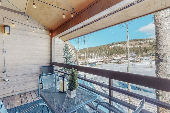 A balcony with a wooden ceiling, metal chairs, a table, and a potted plant. - Best Ski in Ski out Location in Angel Fire! (Angel Fire)