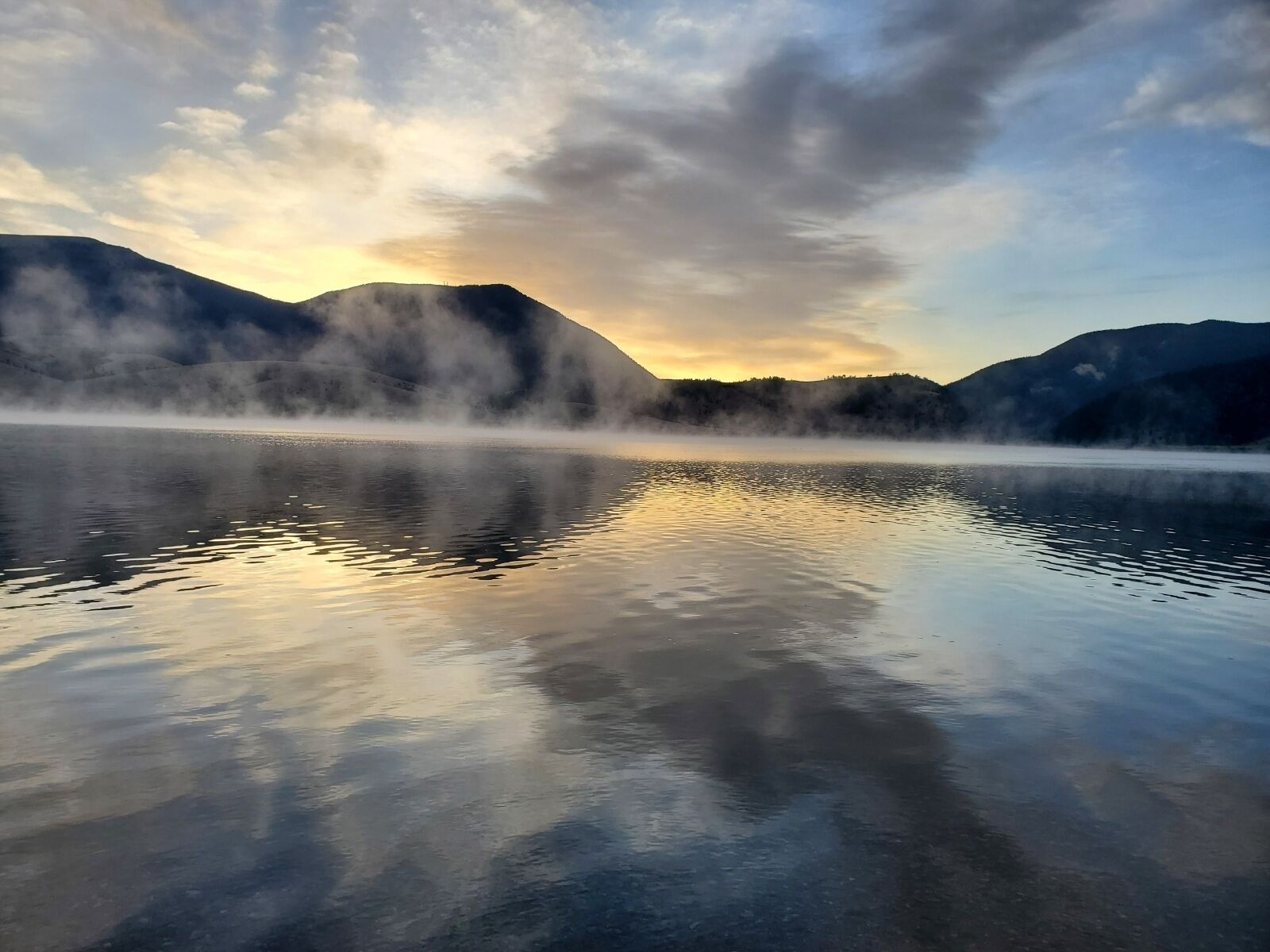 Un lac paisible, avec des montagnes en arrière-plan et une atmosphère brumeuse.