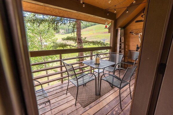 A wooden deck with metal chairs and a table, overlooking a grassy area with trees. - Best Ski in Ski out Location in Angel Fire! (Angel Fire)