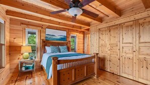 Un dormitori de cabana de fusta amb un llit, una tauleta de nit, una làmpada i un ventilador de sostre.