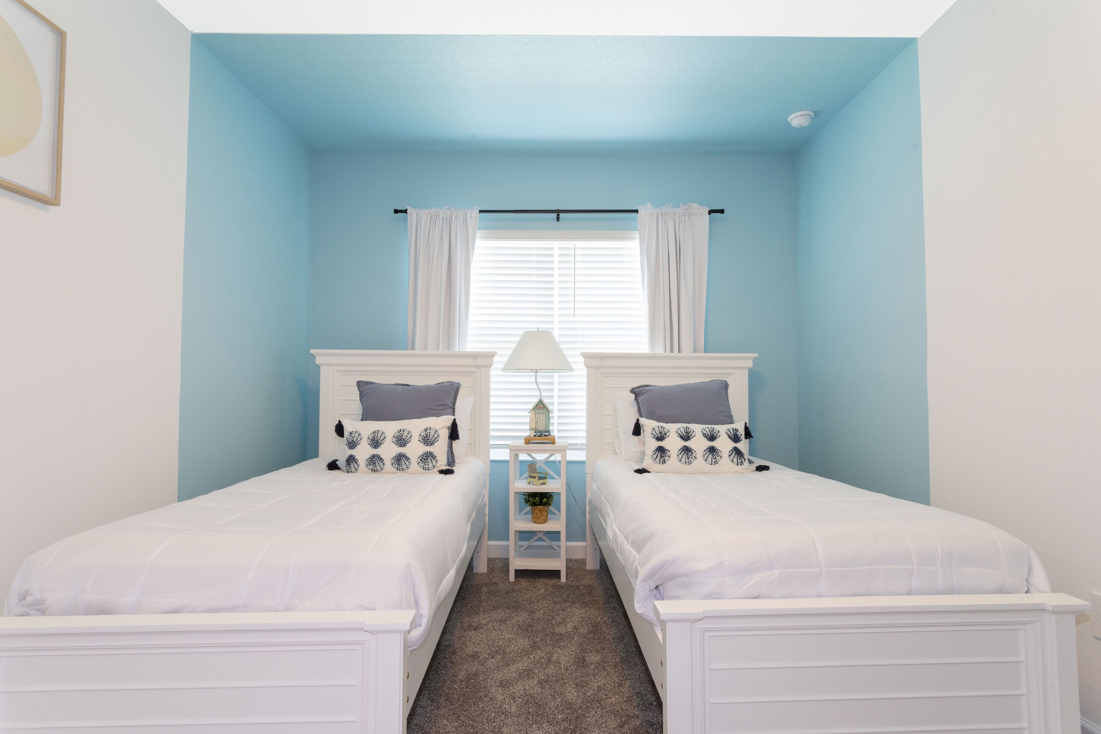 A bedroom with two beds, a nightstand, a lamp, and a window with curtains.