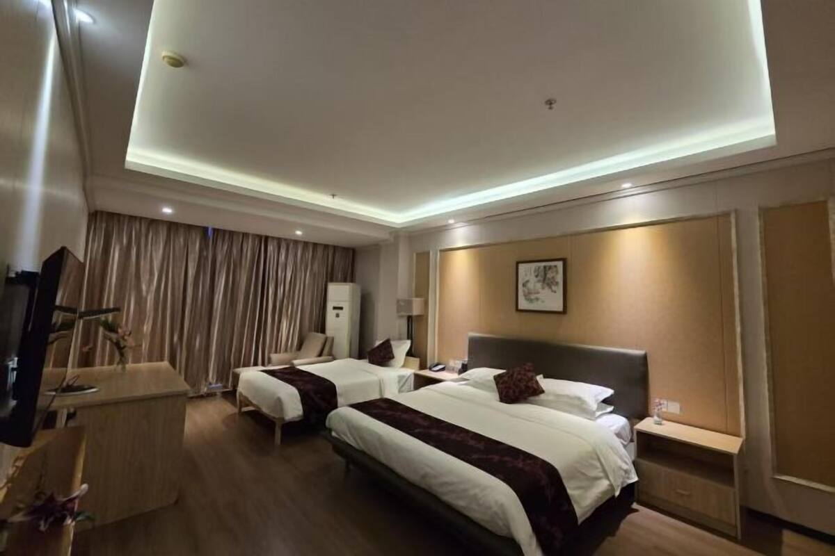 A hotel room with two beds, a desk, a television, and a ceiling light.
