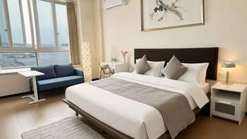 A hotel room with a large bed, a desk, a chair, and a view of the city.