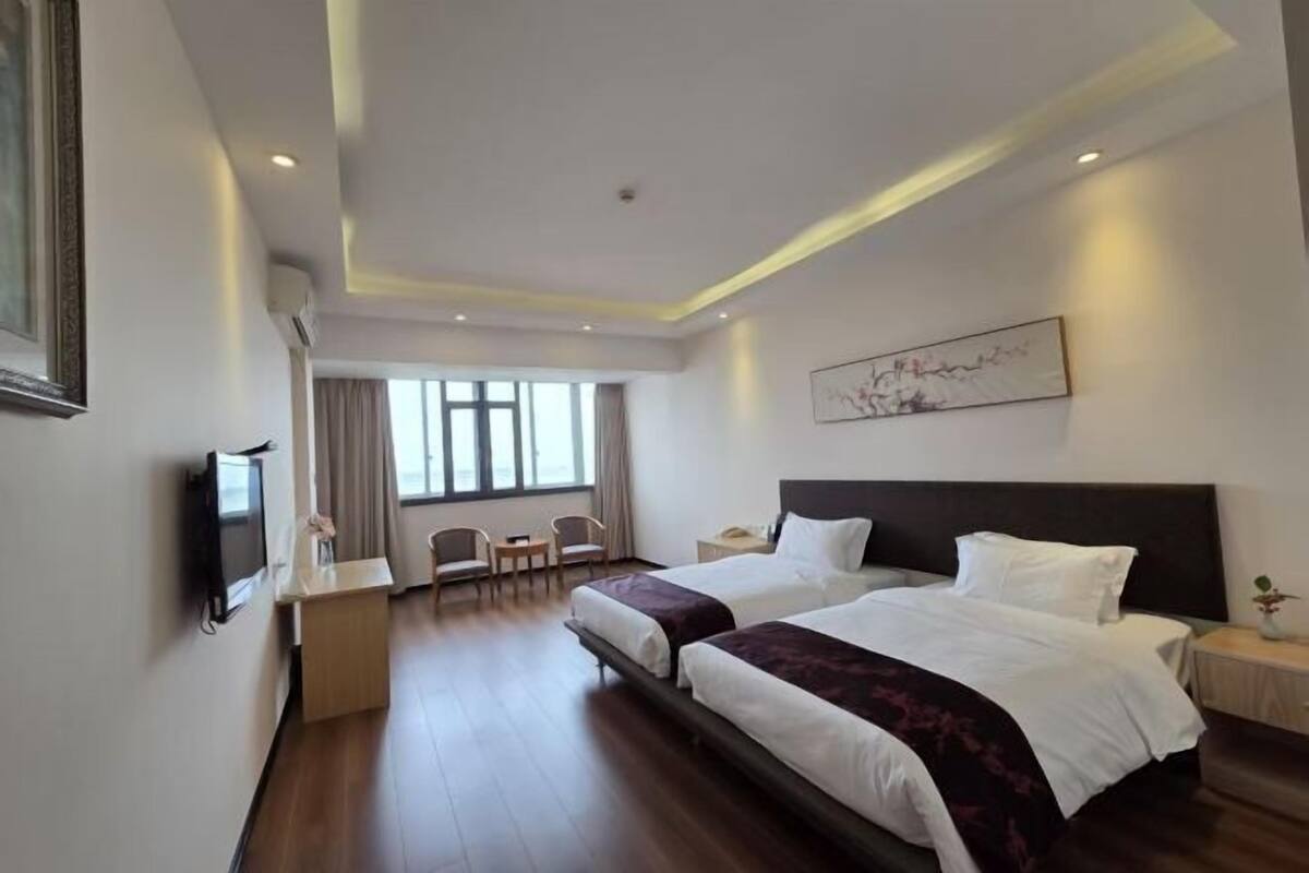A hotel room with two beds, a desk, a chair, a TV, and a window.